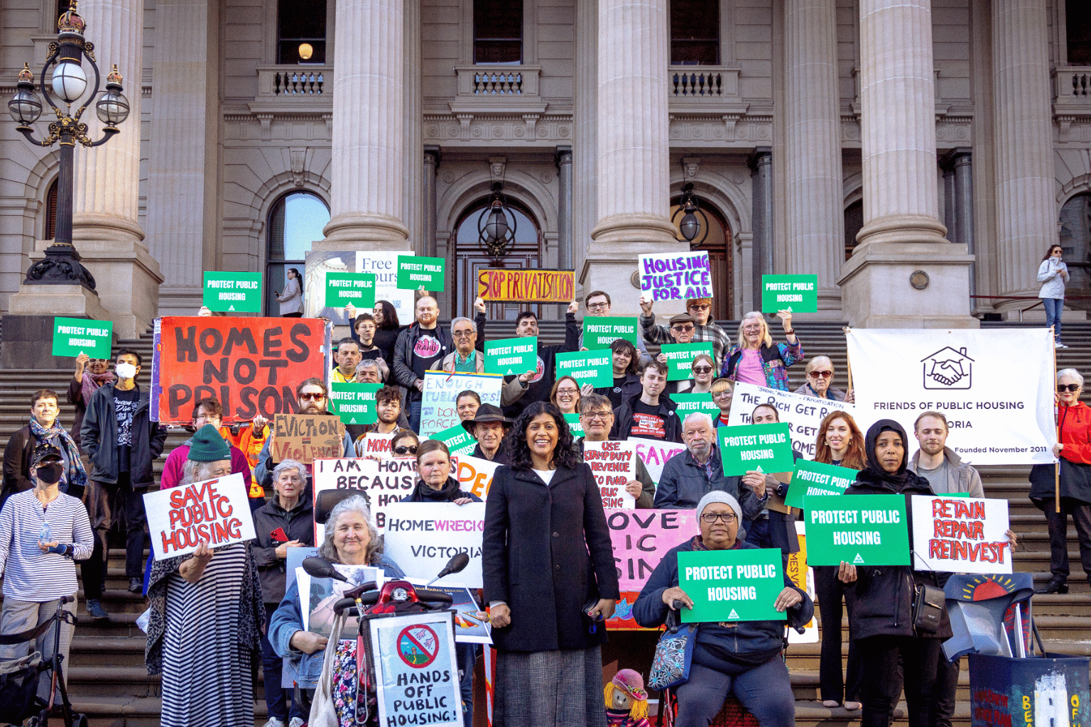 Group of public housing protestors on parliament steps with Samantha Ratnam at the front of the group.